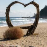 A rustic heart-shaped driftwood sculpture on a sunny Sokcho beach with waves in the background.